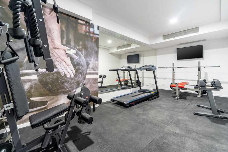 Well-equipped gym with a Treadmill, a Multifunction device, a Bench with some weights, and a TV