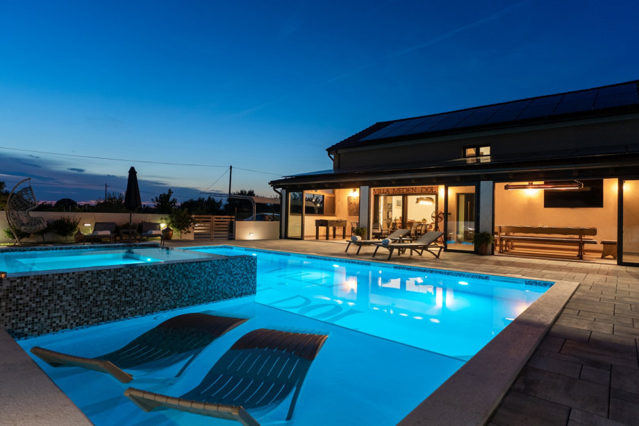 9 x 6.5 meter heated pool with shallow sections and four partially submerged deck chairs