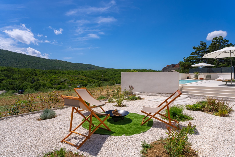 For those seeking a cozy evening ambiance, a few steps away lies a charming fire pit area adorned with plush loungers