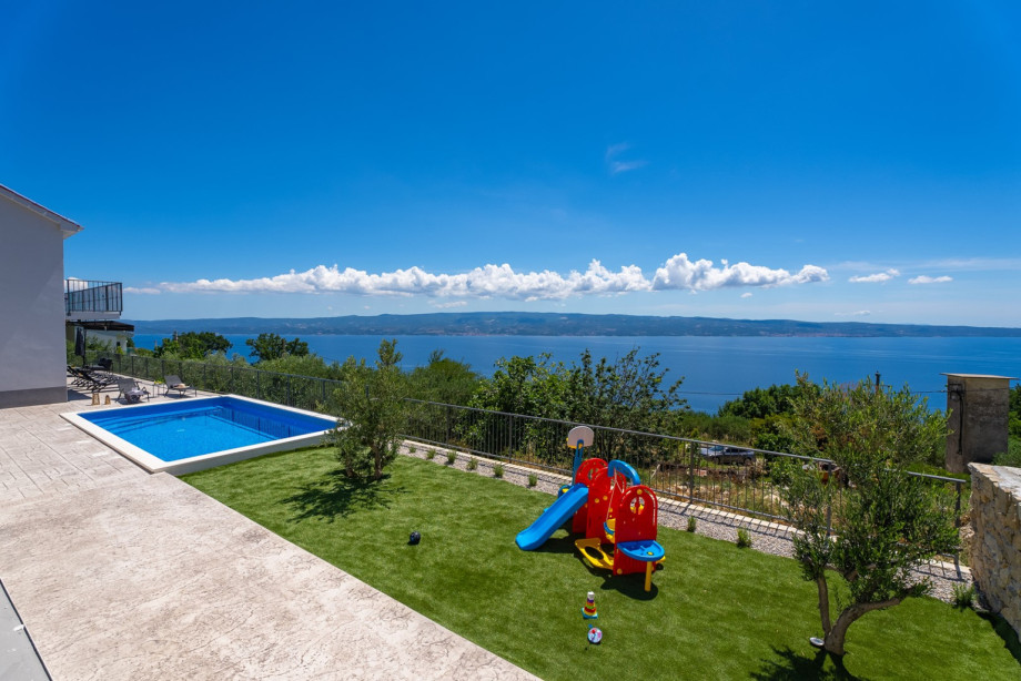 Next  to the pool area is a kid-friendly outdoor playground with a slide, swing, and other toys,
