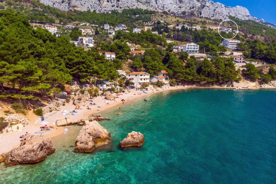 An aerial shot showcases the villa's exclusive, elevated location in Mimice, above the pebbled beach and the clear, blue sea