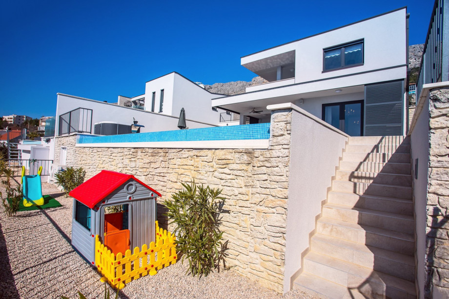 Children corner below the pool area, fenced with small trampoline, house, slide